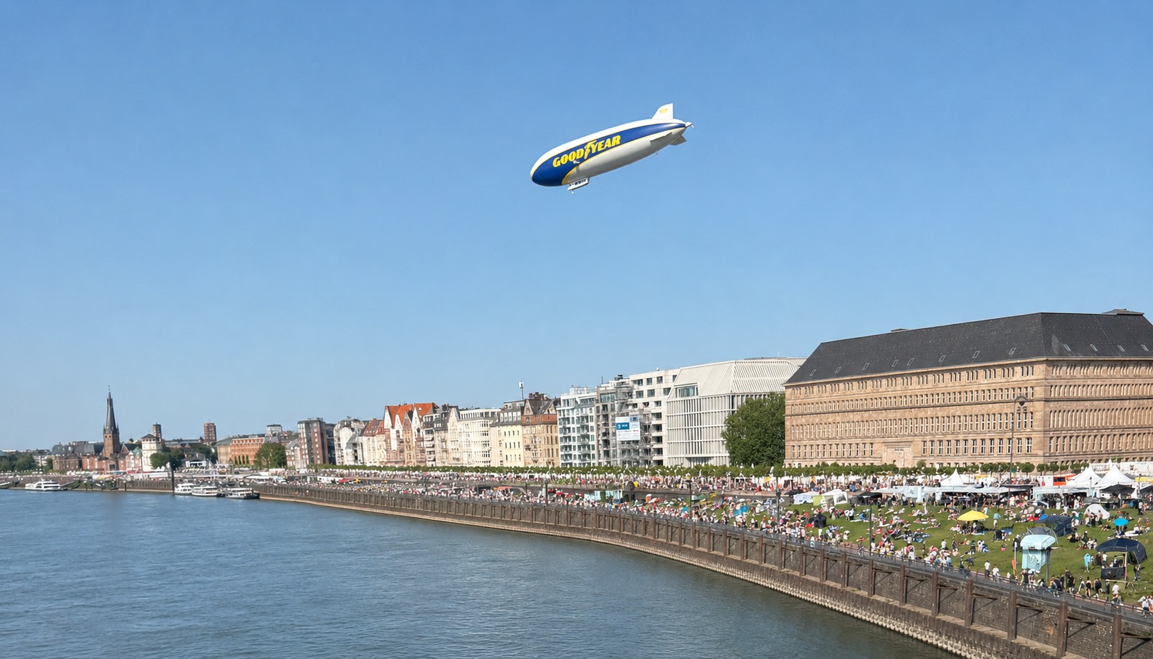 Luftschiff mit Good-Year-Werbung über der mit Menschen gefüllten Rheinpromenade, Rhein, blauer Himmel